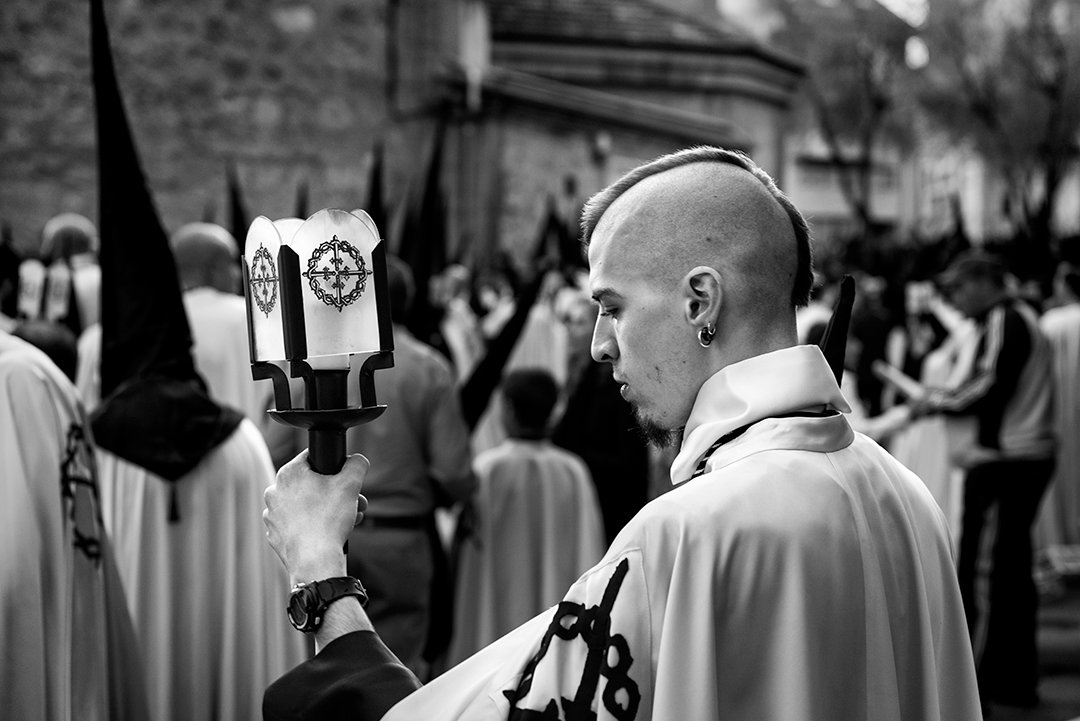 Un joven con túnica blanca entre participantes de una procesión.
